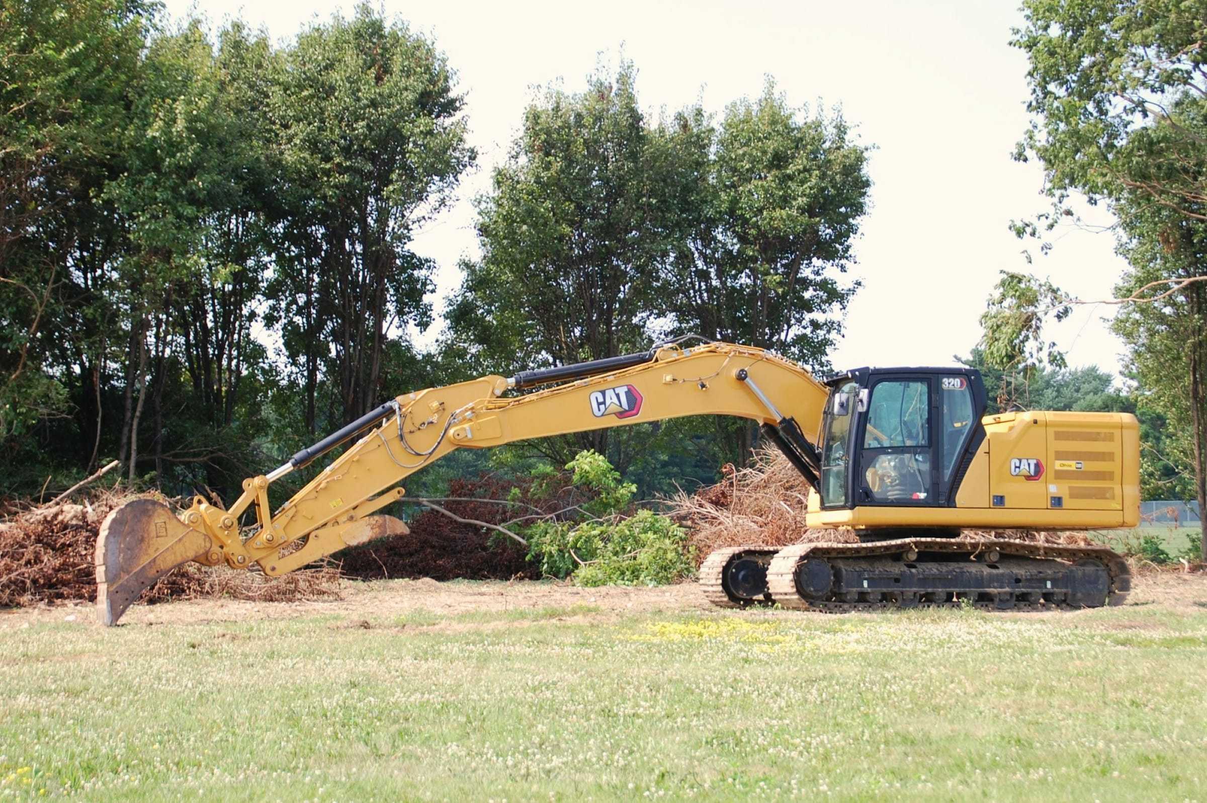 Excavator clearing brush piles on an open lot